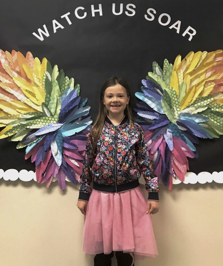 A little girl stands proudly in front of handmade butterfly wings