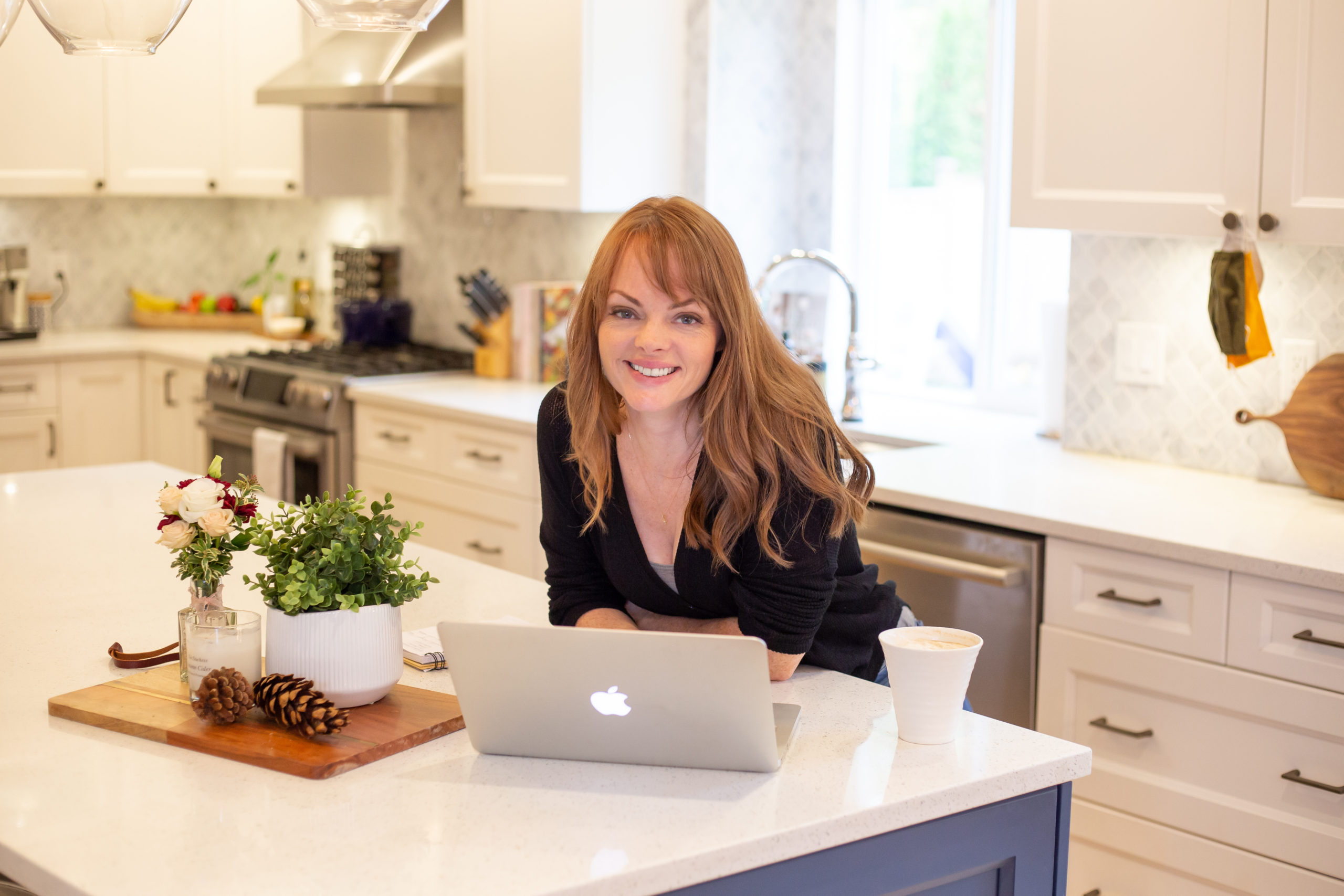 Christine Coughlin leaning on her kitchen island with a laptop in front of her, smiling at the camera