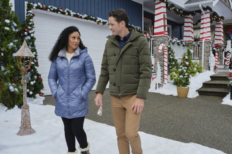 Tamara Mowry-Housley and Paul Campbell are talking as they walk in front of a house that's decorated for Christmas