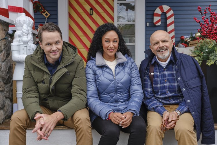 Tamara Mowry-Housley, Paul Campbell and Joe Pantoliano sit on the front porch steps smiling at the camera infant of a house that is decorated for Christmas. How to rent your home as a filming location