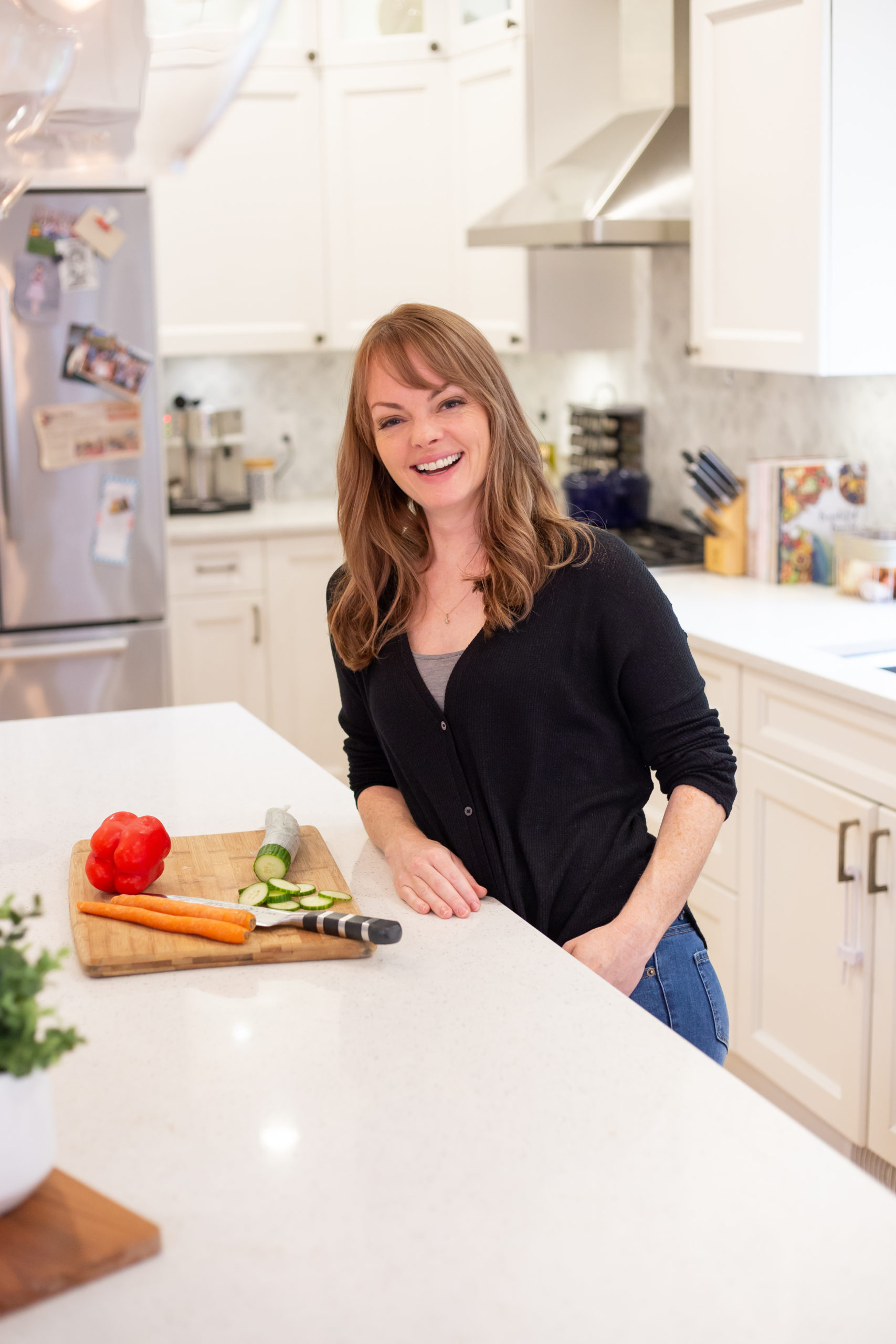 Christine Coughlin leaning against her kitchen island smiling at the camera, fresh veggies sit on the counter.